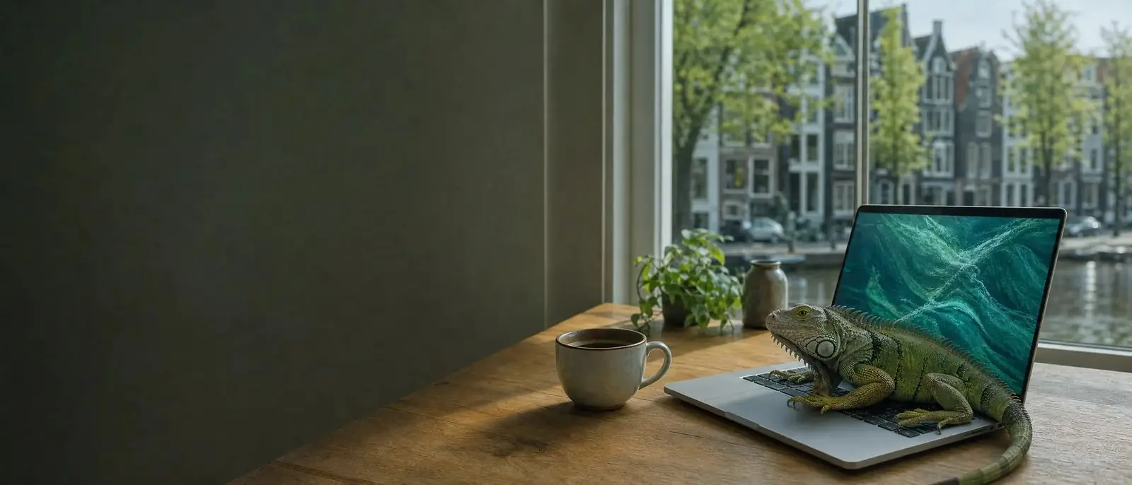 Schreibtisch am Fenster mit Laptop, Kaffeetasse und einem grünen Leguan auf der Tastatur, draußen Grachtenhäuser.